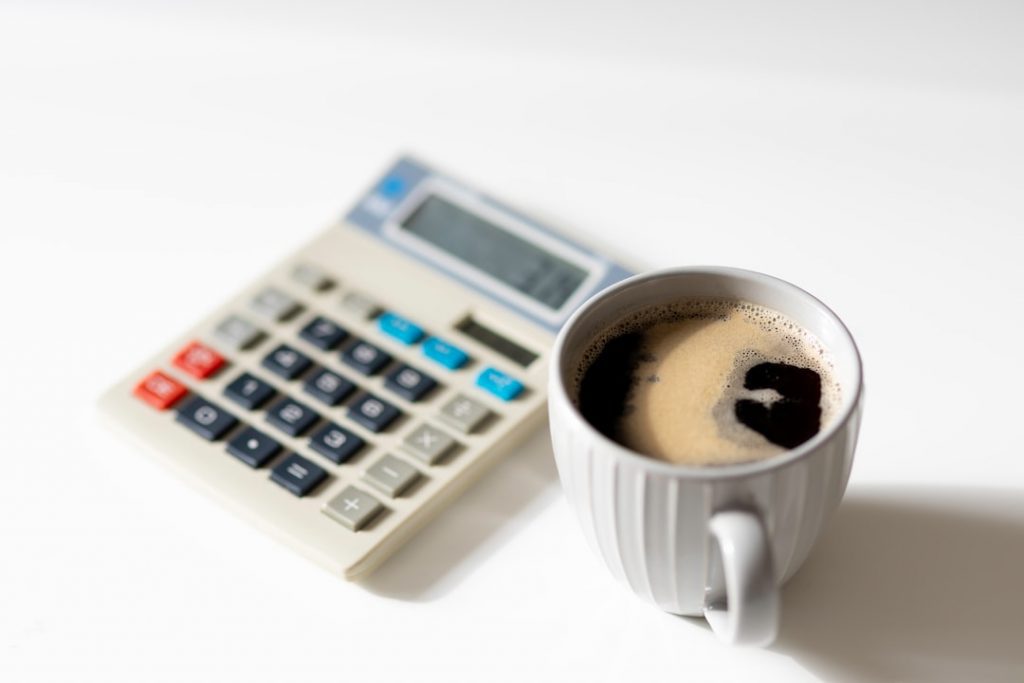 A white mug filled with coffee sits on a white surface next to a calculator, suggesting a work or study setting.