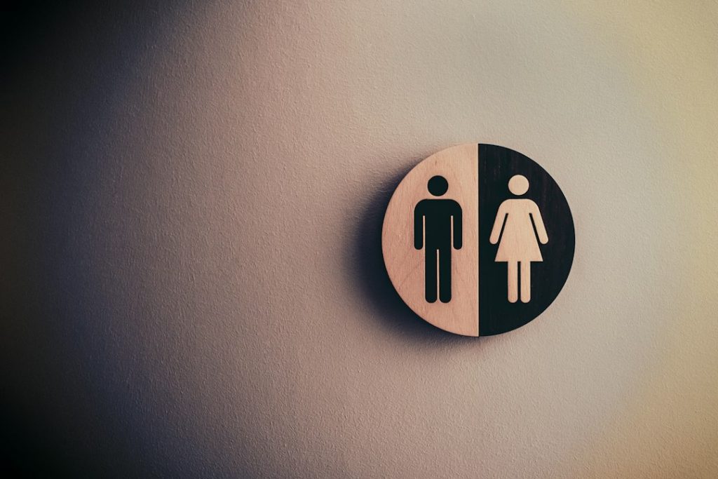 A round toilet sign on a wall, divided in half with male and female symbols, each side featuring a different background colour.