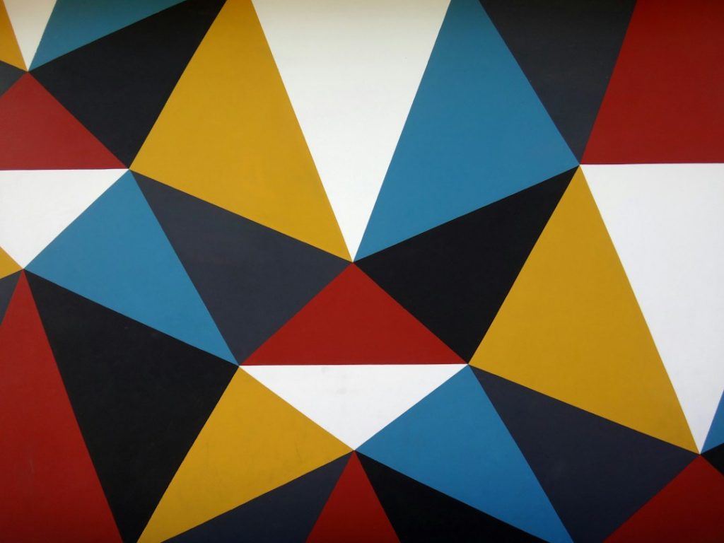 A geometric pattern of triangles in blue, black, red, yellow, and white arranged in a repeating mosaic across the surface, creating a vibrant, abstract design.