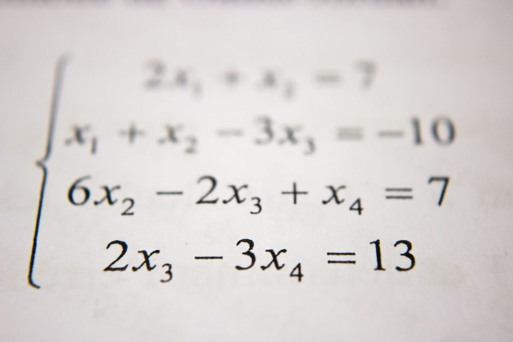 A close-up of a printed page showing a system of four algebraic equations with variables x₁, x₂, x₃, and x₄ in mathematical notation.