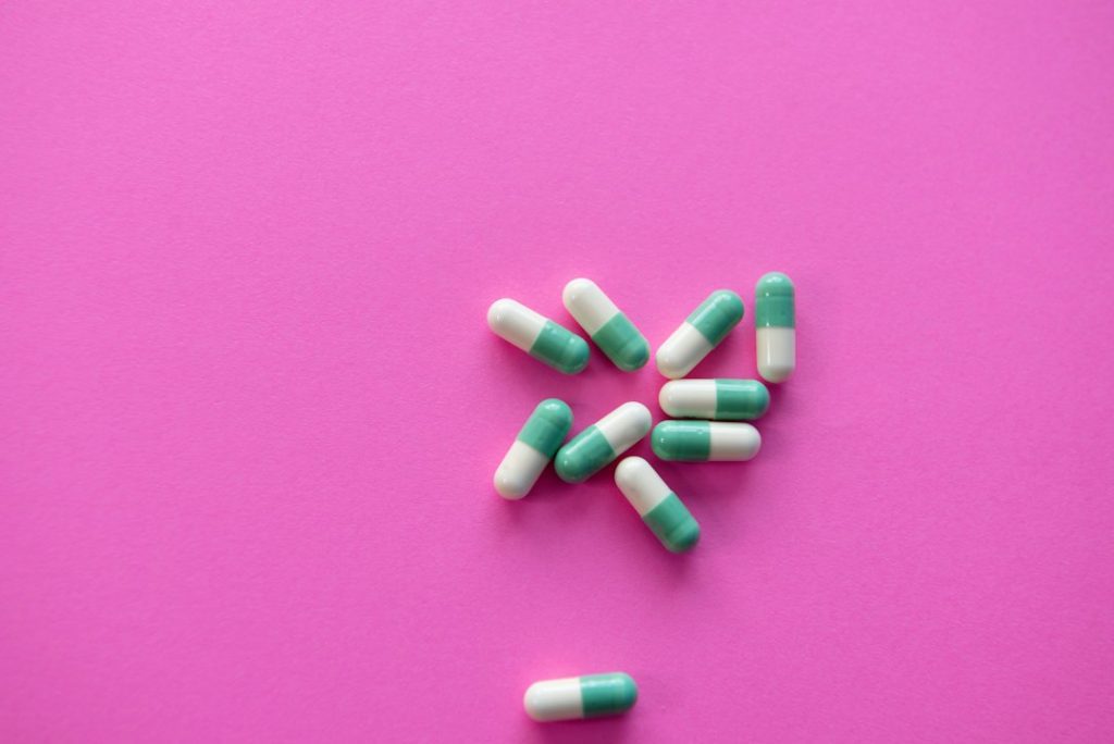 A cluster of green and white capsules scattered on a bright pink background.