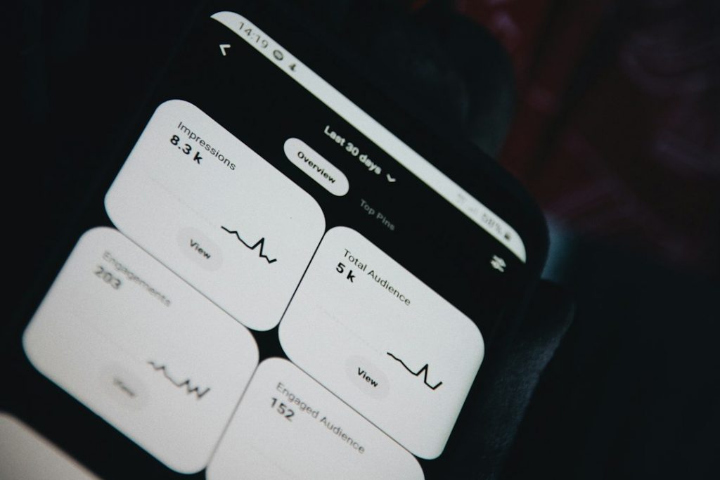 A smartphone screen displays social media analytics, showing metrics like impressions, total audience, engagements, and engaged audience with line graphs and number values for the past 30 days.