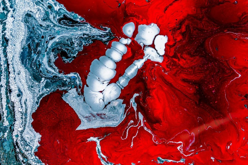 Abstract image featuring swirling red, black, and white colours. The white area forms an irregular, bubble-like shape in the centre, surrounded by bold red and marbled layers, creating a fluid, dynamic pattern.