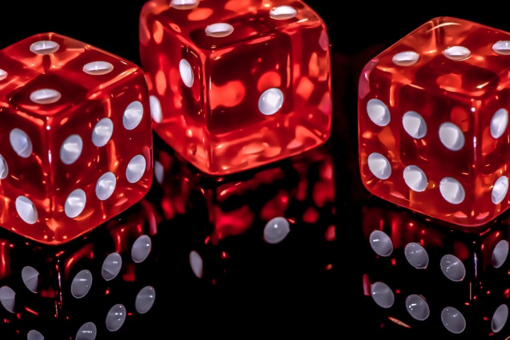 Three red translucent dice with white dots are shown on a glossy black surface, reflecting the dice’s images and dots clearly below them.