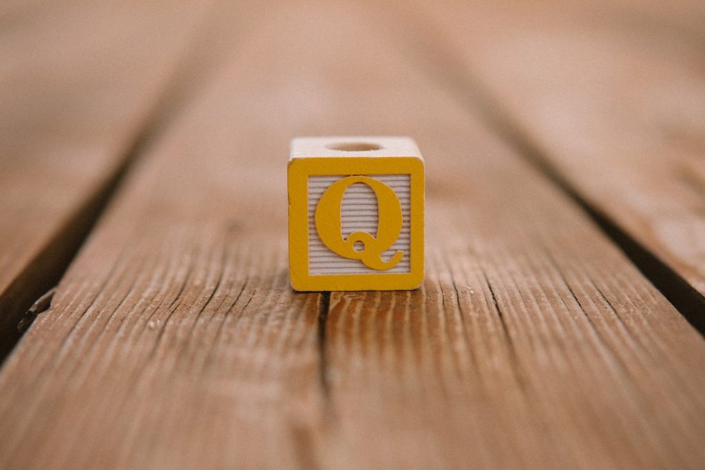 A yellow toy block with the letter Q printed on it sits on a wooden surface with visible grain lines.