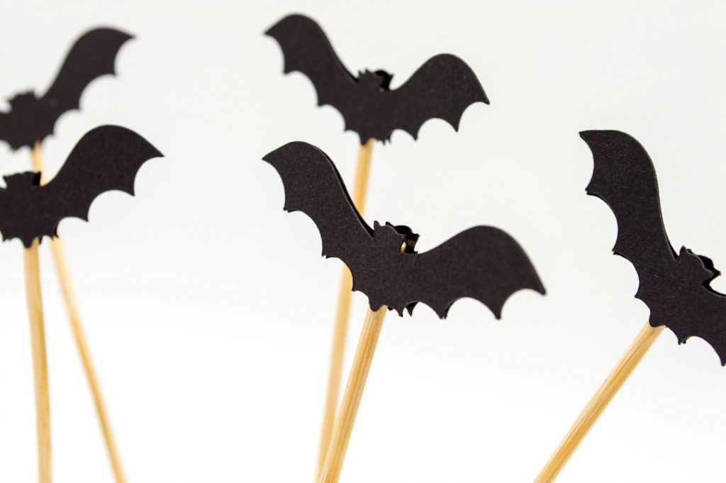Several black paper bats attached to wooden sticks, arranged upright against a plain white background. The bats are silhouetted, giving a decorative, Hallowe’en-themed appearance.