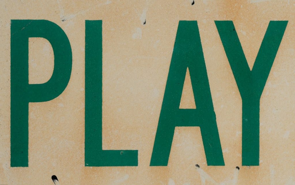 The word PLAY is written in large, green, capital letters on a worn, beige background with small black marks and smudges.