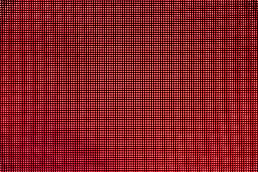 A close-up image of a red LED screen displaying a grid of tiny, evenly spaced dots, creating a textured and illuminated pattern with gradual shading from light to dark red.