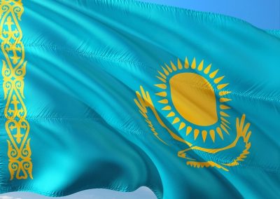 The flag of Kazakhstan, featuring a sky blue background with a gold sun above a golden steppe eagle in the centre, and a vertical Kazakh ornamental pattern near the hoist side, waves in the wind.