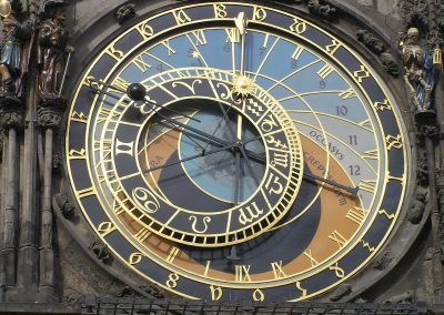 Close-up of the Prague astronomical clock in the Czech Republic, showing detailed golden numbers, zodiac signs, and ornate hands on a colourful circular face, with small decorative figures on either side.