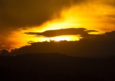 A dramatic sunset with a golden sky, dark clouds partially covering the sun, and silhouetted hills in the foreground.