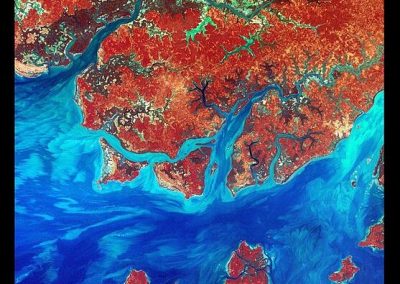 Satellite image of Guinea-Bissau’s coastline with red and orange land areas, winding dark rivers, and blue ocean waters, highlighting the contrast between land and sea. USGS and NASA logos mark this vivid view of Guinea-Bissau in the bottom corners.