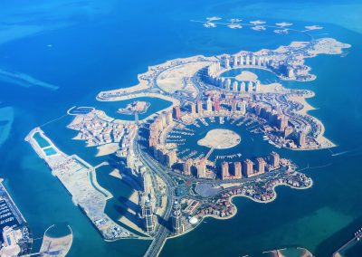Aerial view of The Pearl-Qatar, an artificial island in Qatar featuring circular and spiral-shaped luxury buildings, marinas, and waterfront developments surrounded by turquoise water.