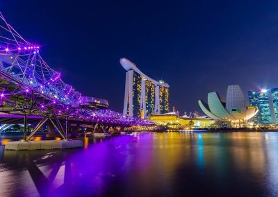 A night view of Singapore’s Marina Bay, featuring the Helix Bridge lit in purple, the Marina Bay Sands hotel, and the ArtScience Museum, all reflecting on the calm Singapore waters.