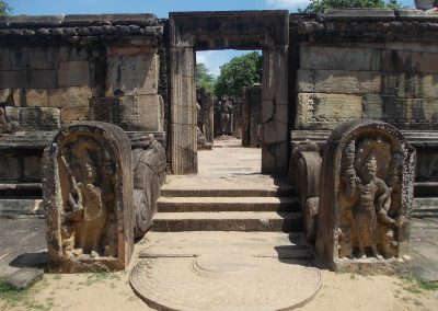 Ancient stone ruins in Sri Lanka with detailed carvings flank a short staircase leading to a doorway; weathered walls and open sky are visible in the background.